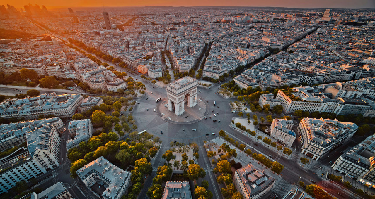 Vista aérea del Arco de Triunfo en el centro de París, con los bulevares bañados por el sol extendiéndose por la ciudad al atardecer.