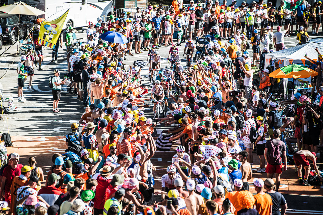 Una multitud llena una carretera estrecha animando a los ciclistas durante la carrera.