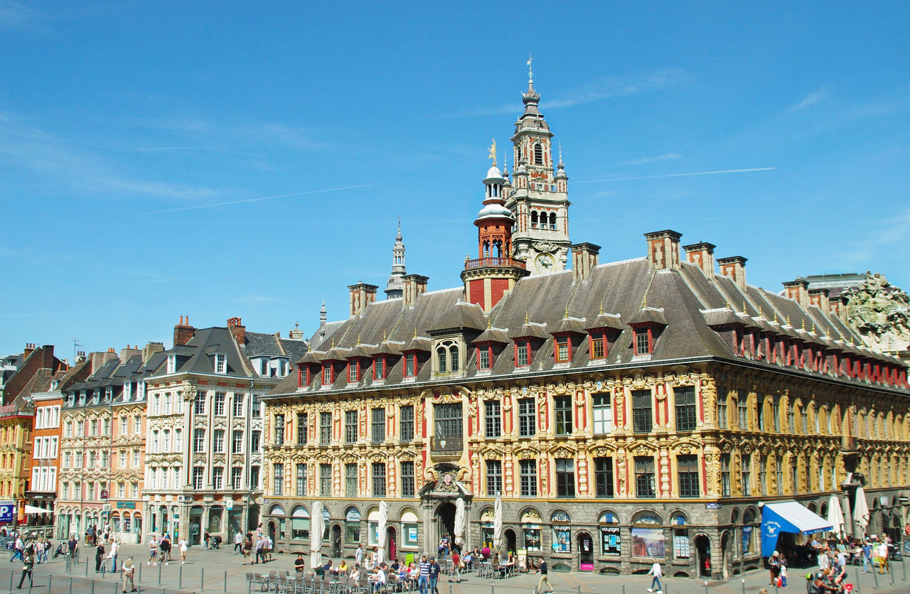 El edificio ornamentado de la Vieille Bourse y la arquitectura circundante de estilo flamenco en la Grand Place de Lille bajo un cielo azul despejado.