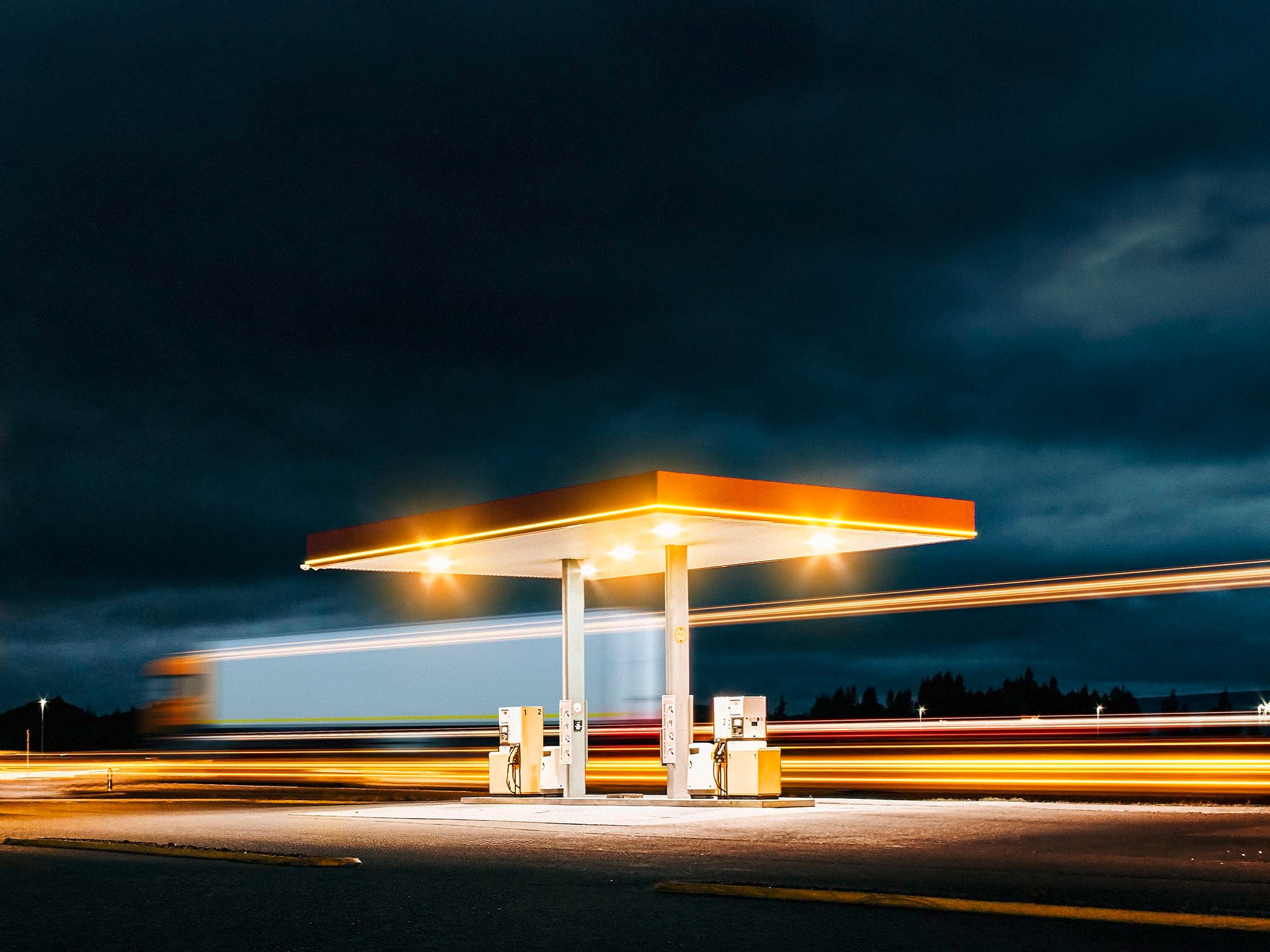 A Truck passes a gas station during night.