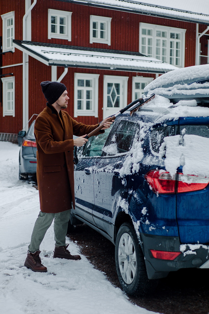 A man cleaning his car from snow in front of a house.